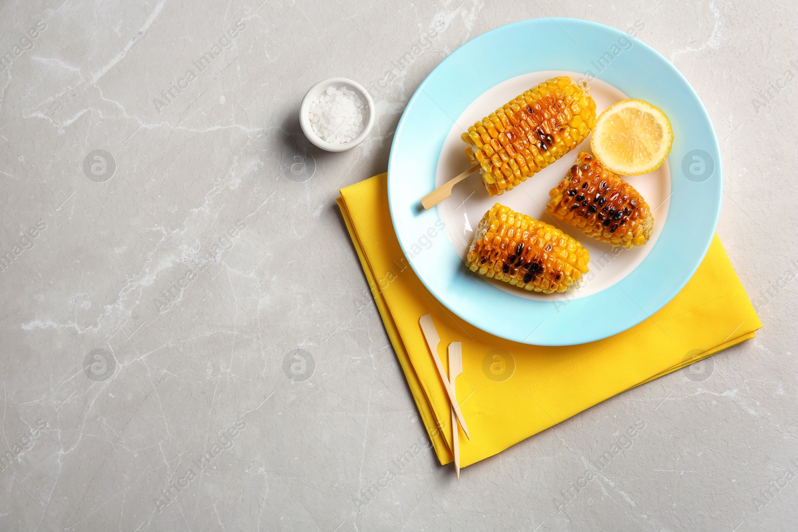 Photo of Plate with delicious grilled corn cobs on light table, top view. Space for text