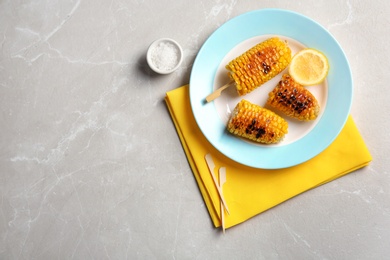 Photo of Plate with delicious grilled corn cobs on light table, top view. Space for text