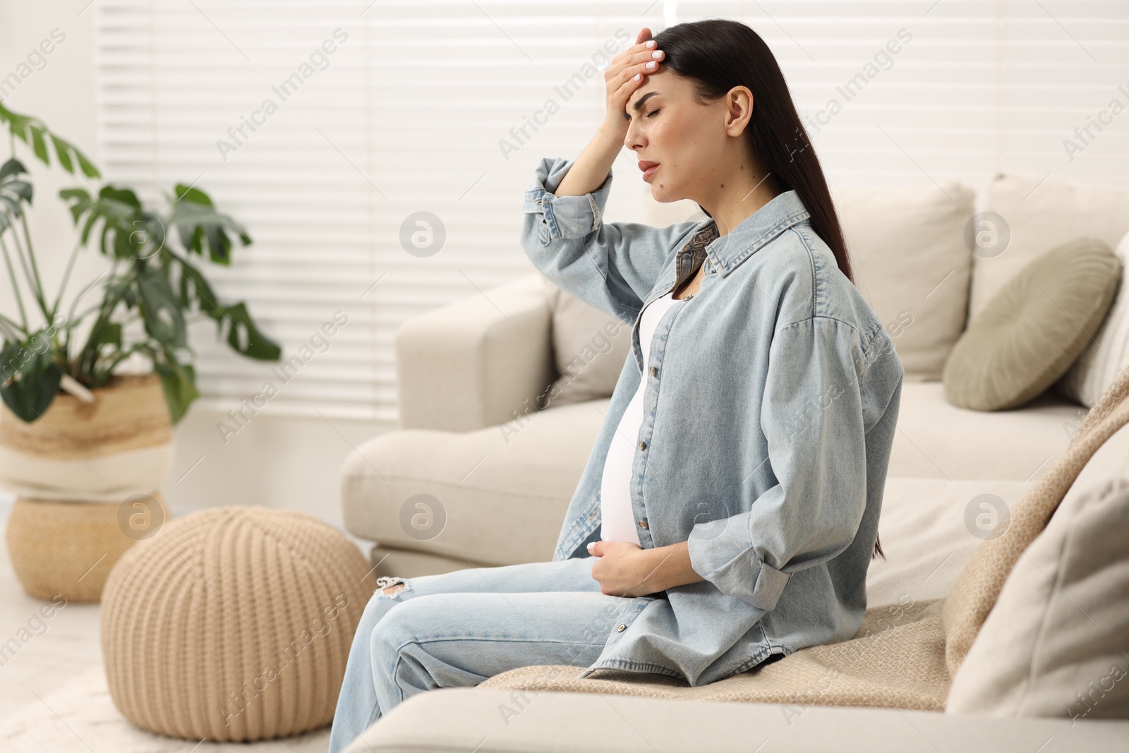 Photo of Pregnant woman suffering from headache on sofa at home