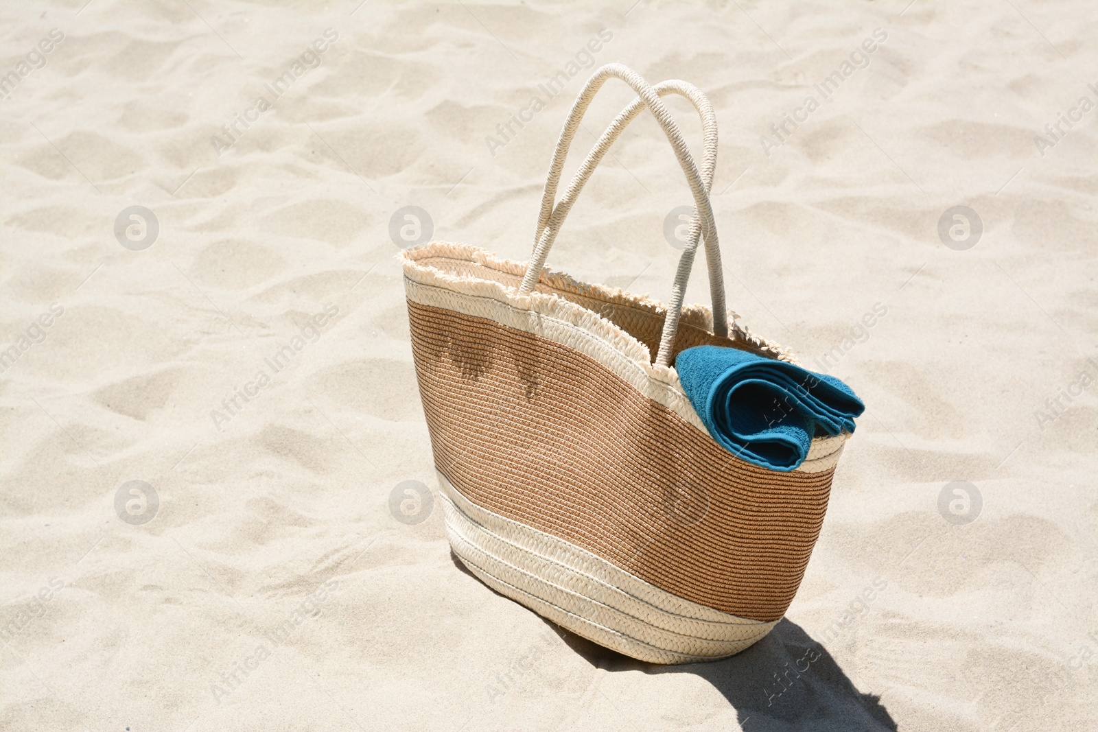 Photo of Soft blue towel in beach bag on sand