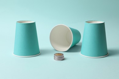 Three paper cups and coins on light blue background. Thimblerig game