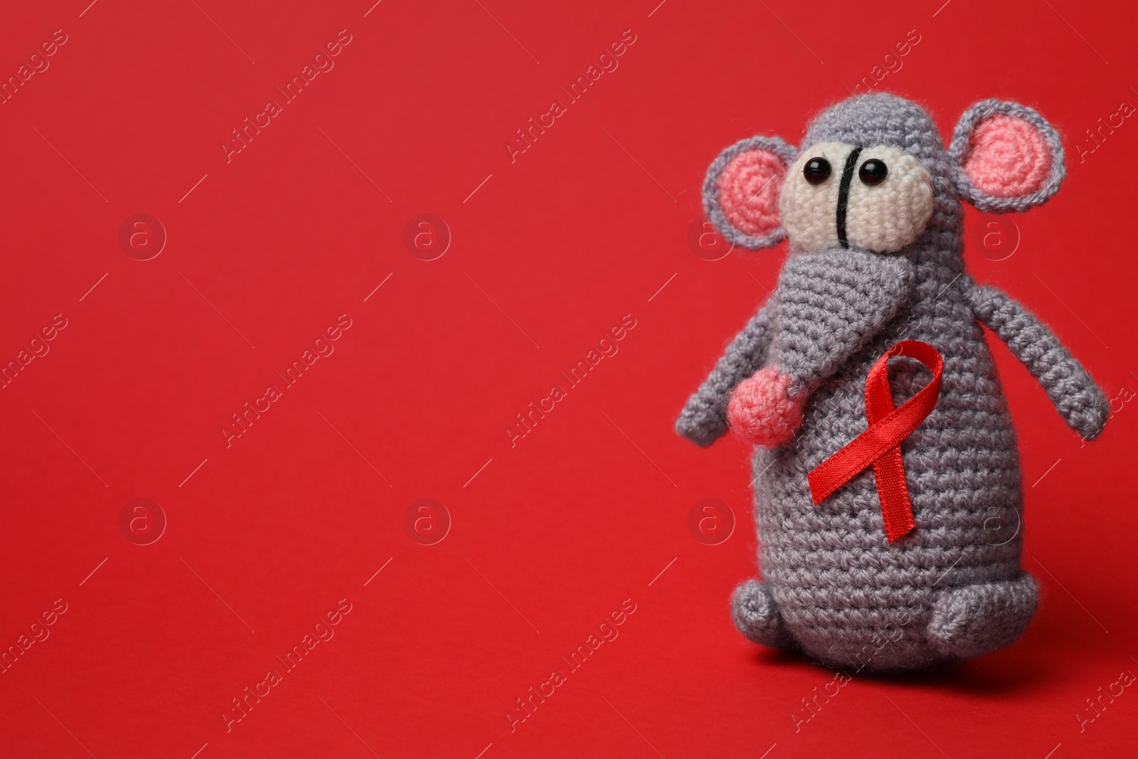 Photo of Cute knitted toy mouse with ribbon on red background, space for text. AIDS disease awareness