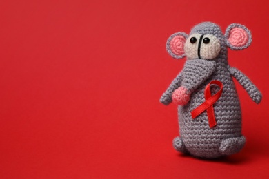 Photo of Cute knitted toy mouse with ribbon on red background, space for text. AIDS disease awareness