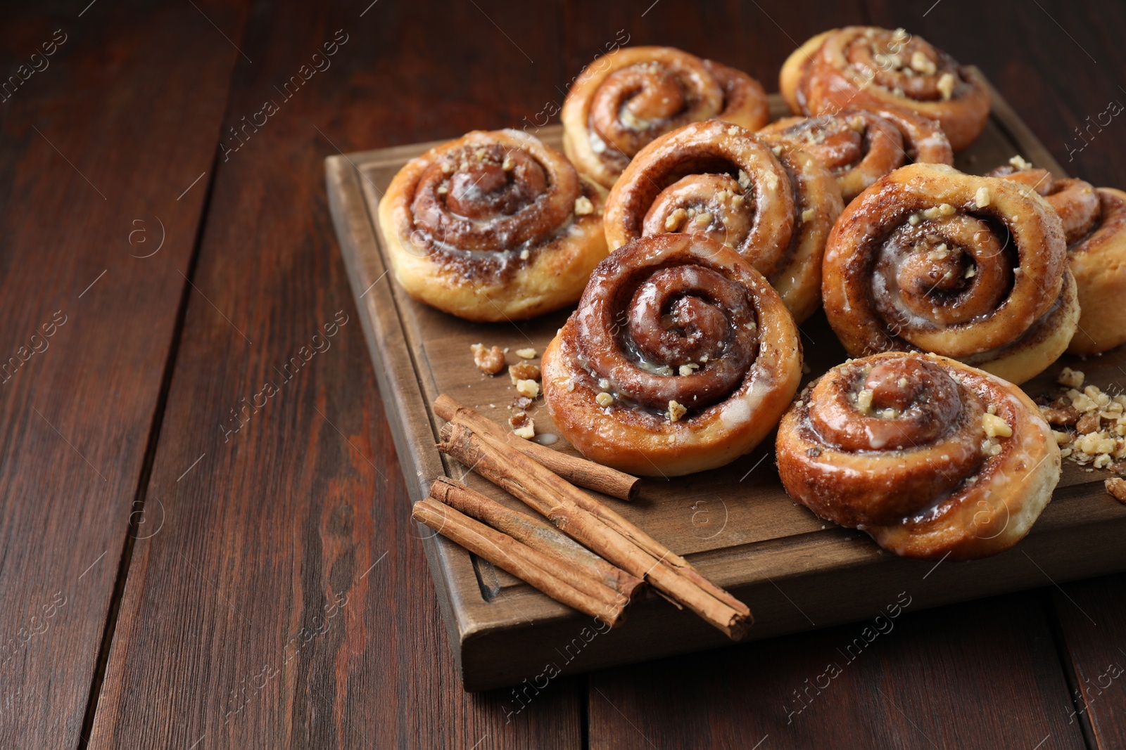 Photo of Tasty cinnamon rolls, sticks and nuts on wooden table, space for text