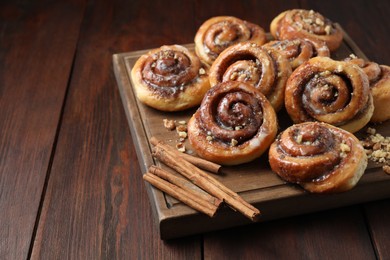 Tasty cinnamon rolls, sticks and nuts on wooden table, space for text