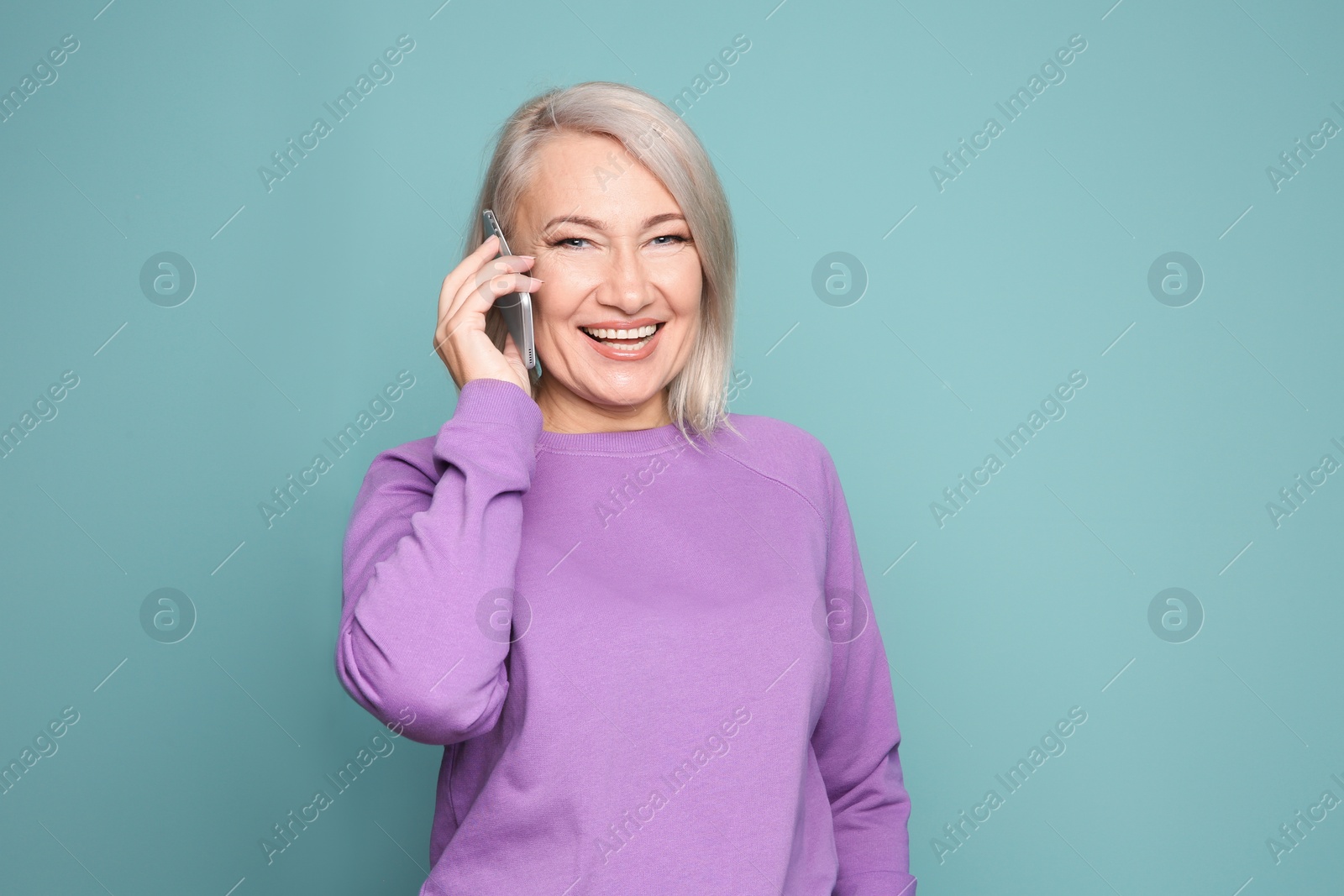 Photo of Mature woman talking on mobile phone against color background