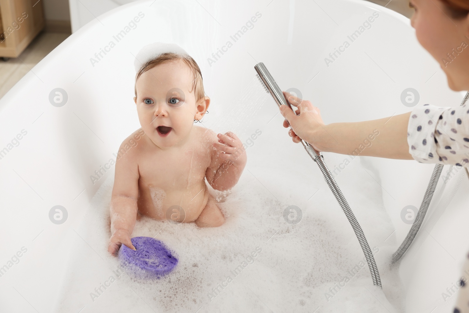 Photo of Mother washing her little baby in tub at home, closeup