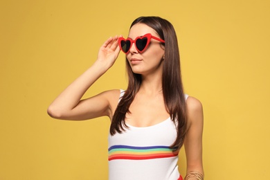 Portrait of beautiful young woman with heart shaped sunglasses on color background