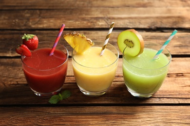 Photo of Delicious colorful juices in glasses on wooden table