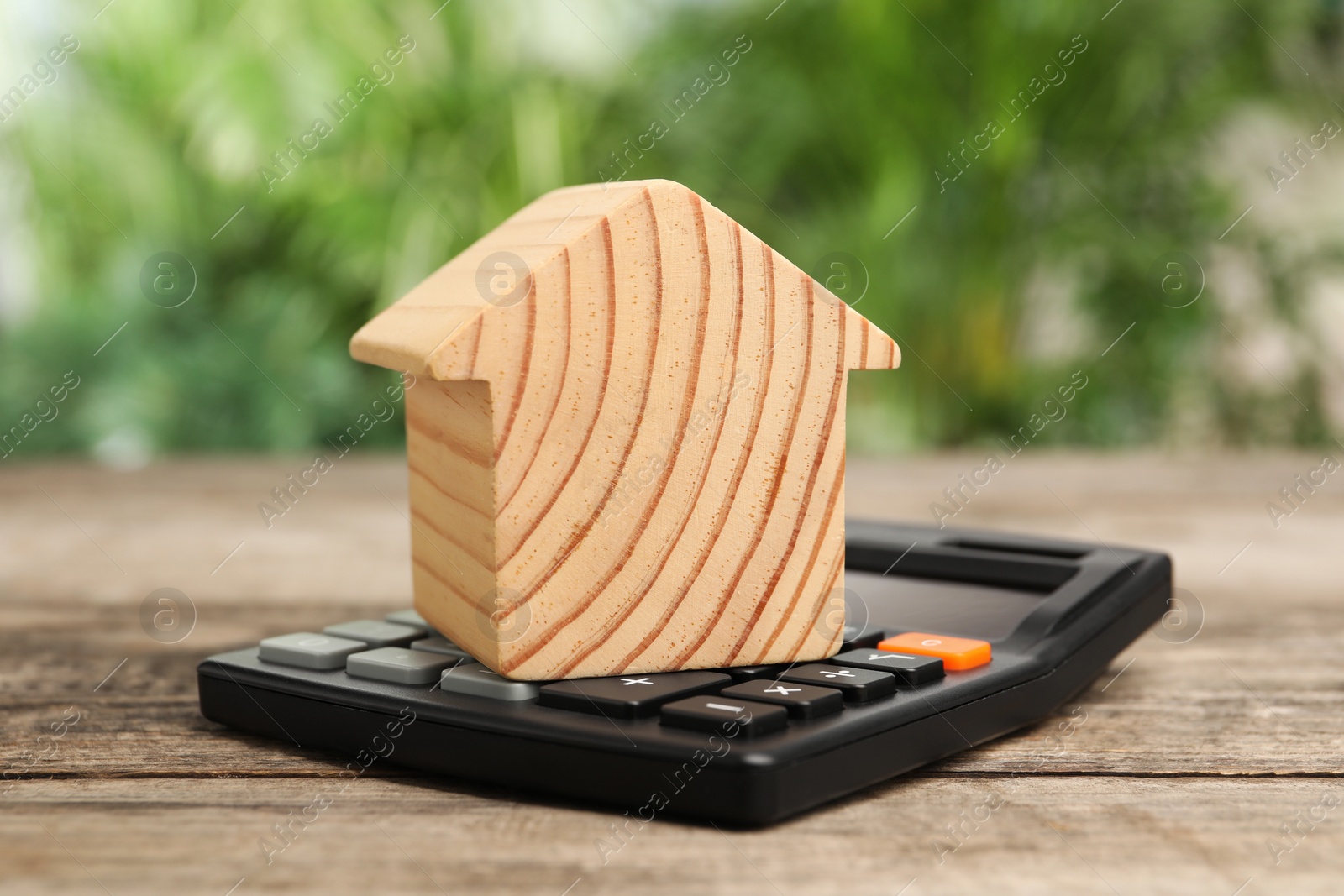 Photo of Mortgage concept. Model house and calculator on wooden table against blurred green background, closeup