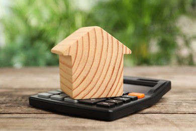 Mortgage concept. Model house and calculator on wooden table against blurred green background, closeup