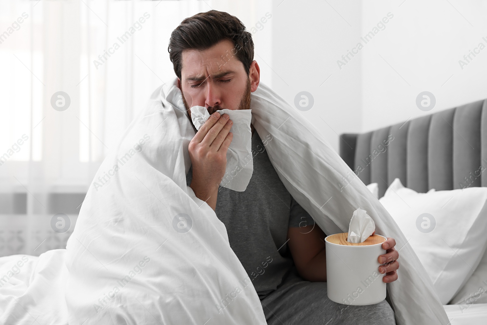 Photo of Sick man with tissue coughing on bed at home. Cold symptoms