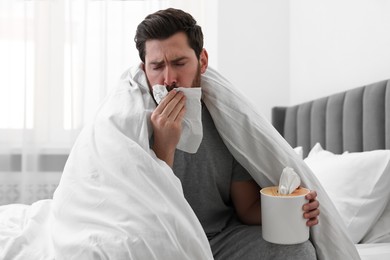 Photo of Sick man with tissue coughing on bed at home. Cold symptoms