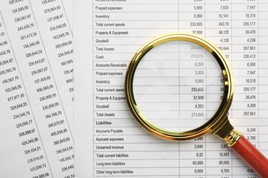Photo of Magnifying glass on accounting documents with data, top view