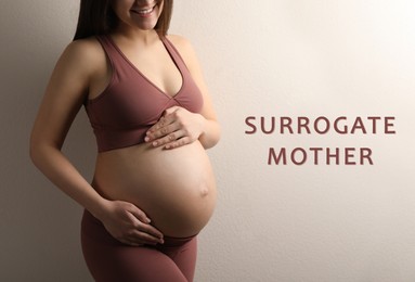 Surrogate mother. Pregnant woman touching her belly on beige background, closeup