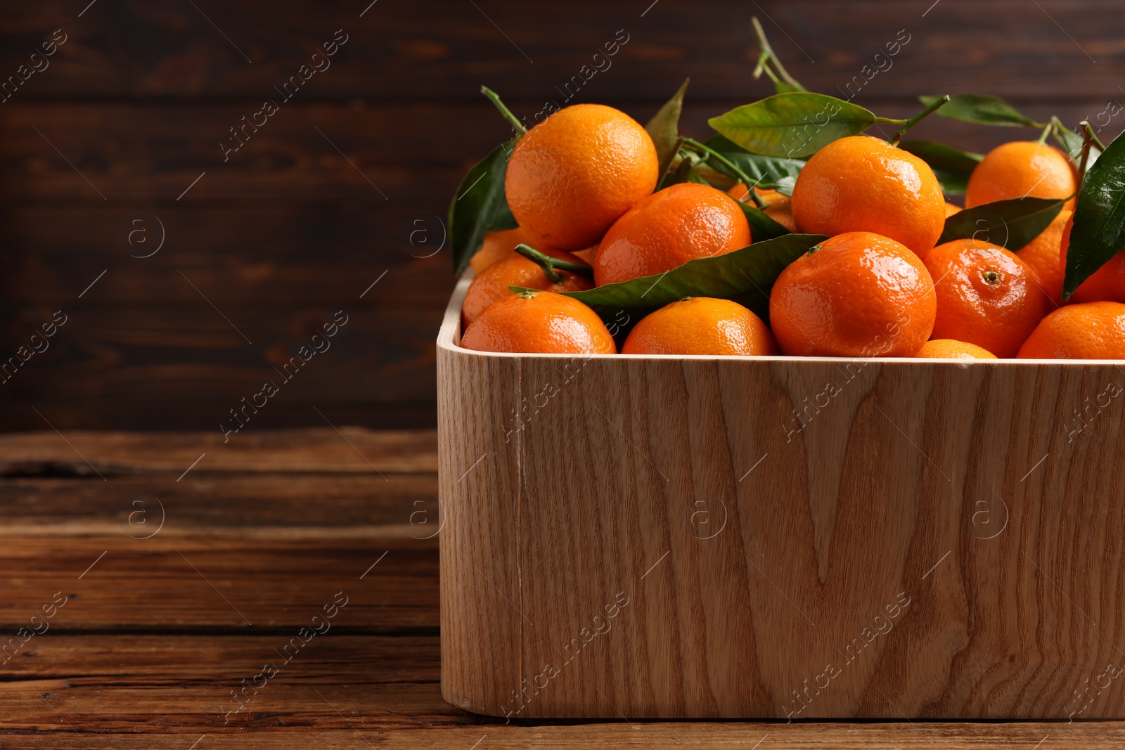 Photo of Fresh tangerines with green leaves in crate on wooden table, closeup. Space for text