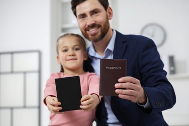 Immigration. Happy man and his daughter with passports indoors, selective focus