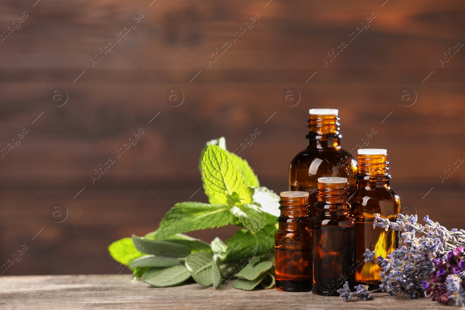 Photo of Bottles with essential oils, herbs and flowers on wooden table. Space for text