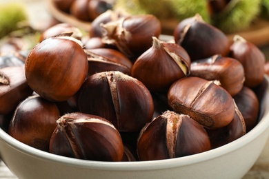 Photo of Delicious roasted edible chestnuts in bowl, closeup