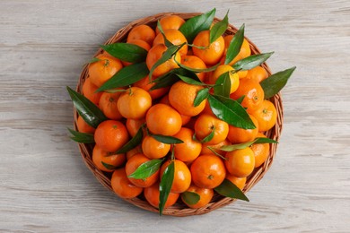 Photo of Fresh ripe juicy tangerines and green leaves on white wooden table, top view
