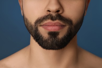 Young man with beard after shaving on blue background, closeup