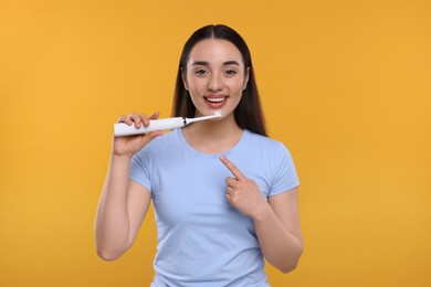 Photo of Happy young woman holding electric toothbrush on yellow background