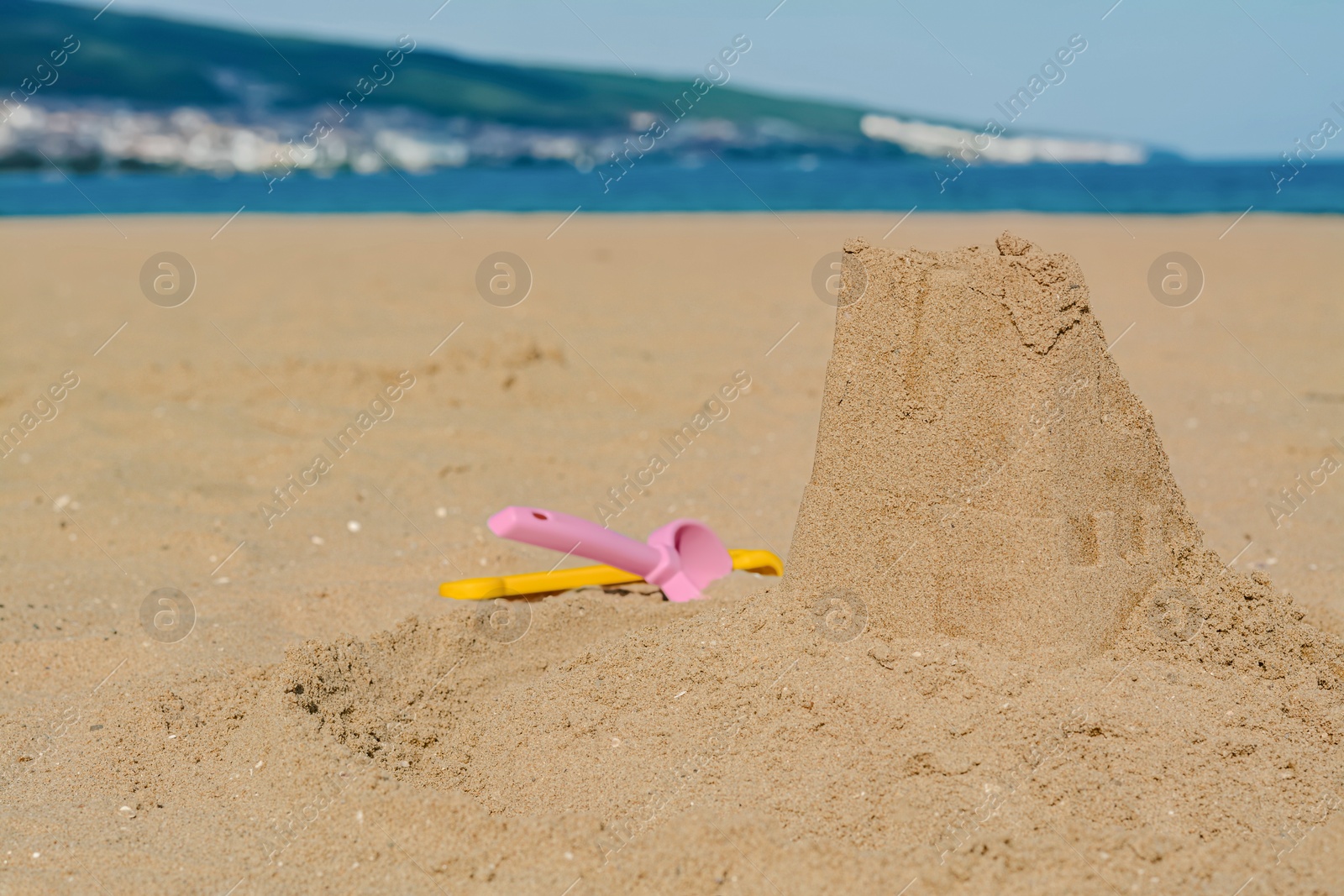 Photo of Beautiful sand castle and plastic toys on beach near sea, space for text