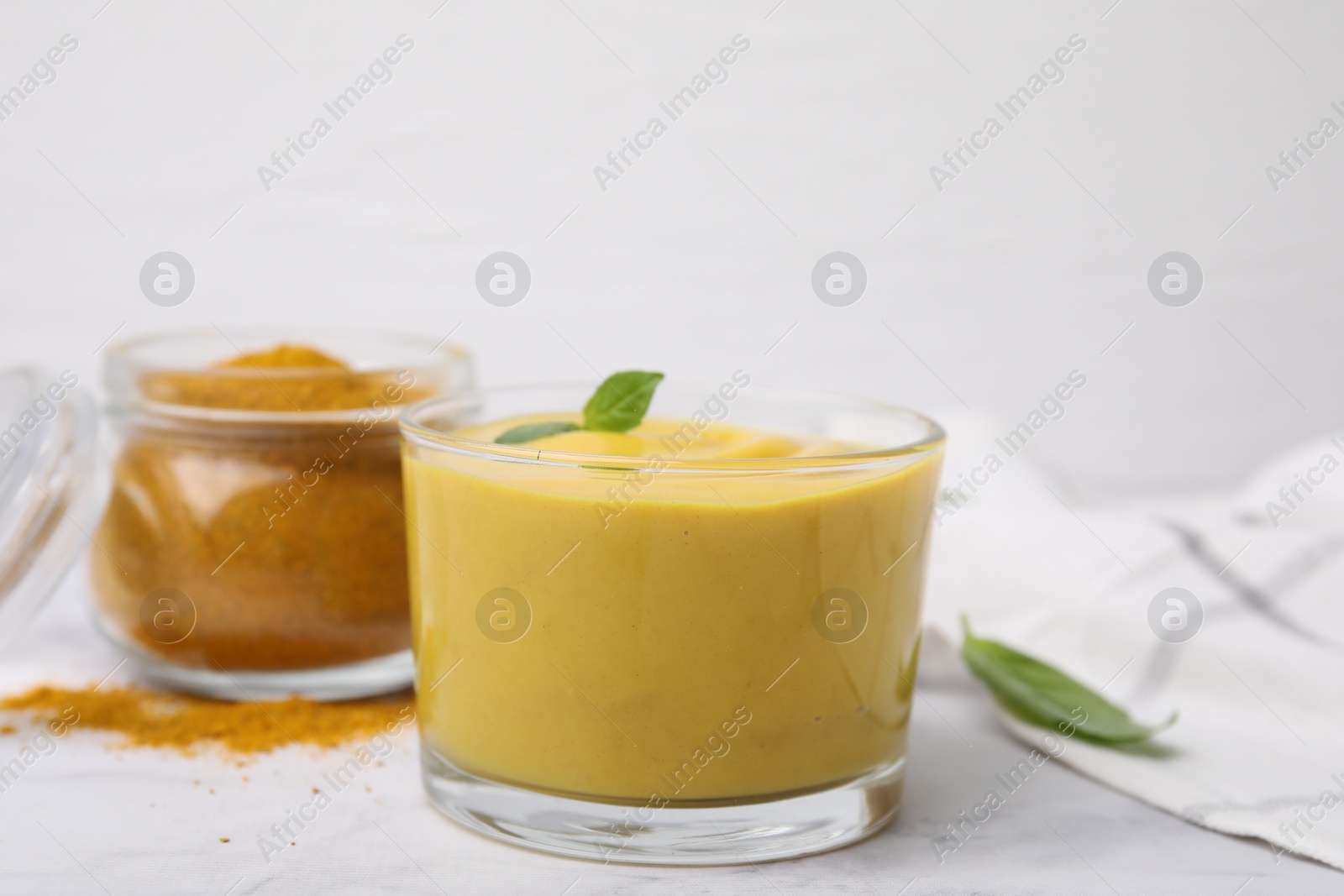 Photo of Tasty curry sauce, powder and basil leaves on white table, closeup