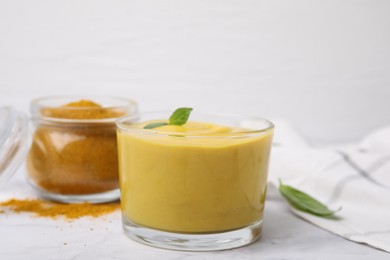 Photo of Tasty curry sauce, powder and basil leaves on white table, closeup