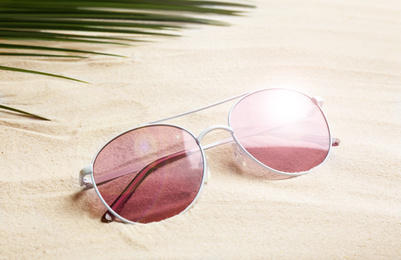 Image of Stylish sunglasses and tropical leaf on white sand. Vacation time