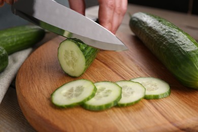 Photo of Woman cutting cucumber on wooden board at table, closeup