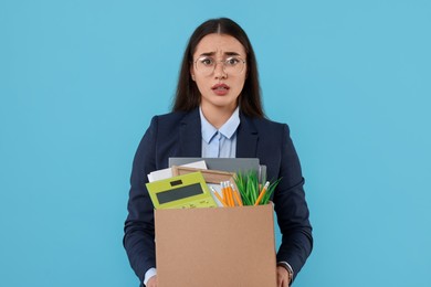 Photo of Unemployment problem. Confused woman with box of personal office belongings on light blue background