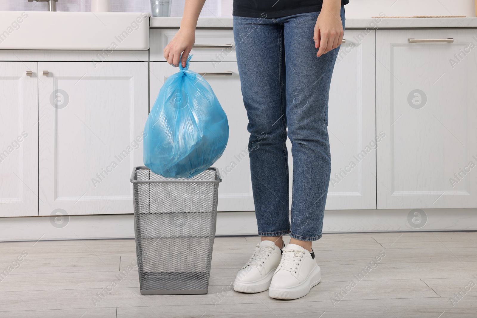 Photo of Woman taking garbage bag out of trash bin in kitchen, closeup