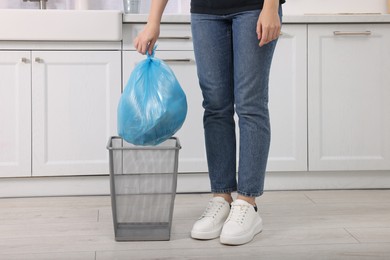 Photo of Woman taking garbage bag out of trash bin in kitchen, closeup