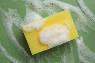 Yellow sponge with foam on green background, top view