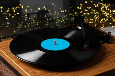 Turntable with vinyl record on wooden table against blurred lights, closeup