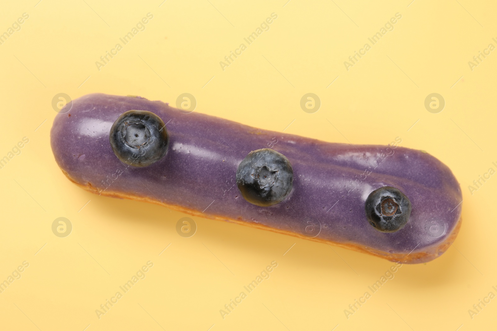 Photo of Delicious purple eclair decorated with blueberries on yellow background, top view