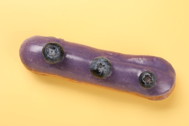 Delicious purple eclair decorated with blueberries on yellow background, top view