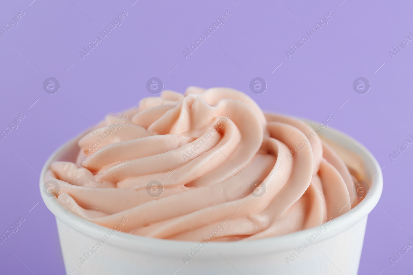 Photo of Cup with tasty frozen yogurt on violet background, closeup