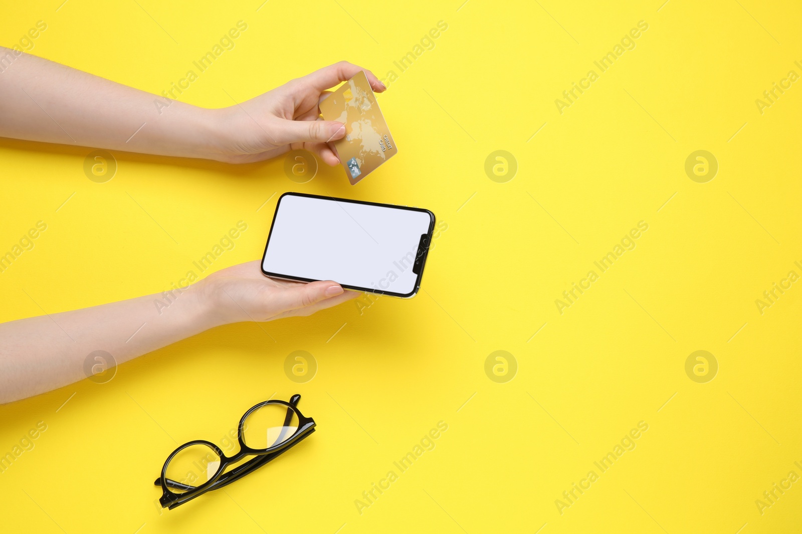 Photo of Online payment. Woman with smartphone, credit card and glasses on yellow background, top view. Space for text