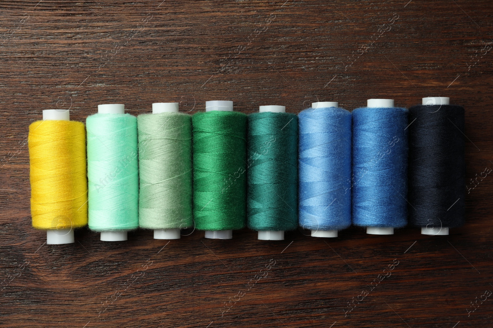 Photo of Set of colorful sewing threads on wooden table, flat lay