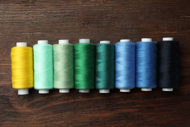 Set of colorful sewing threads on wooden table, flat lay