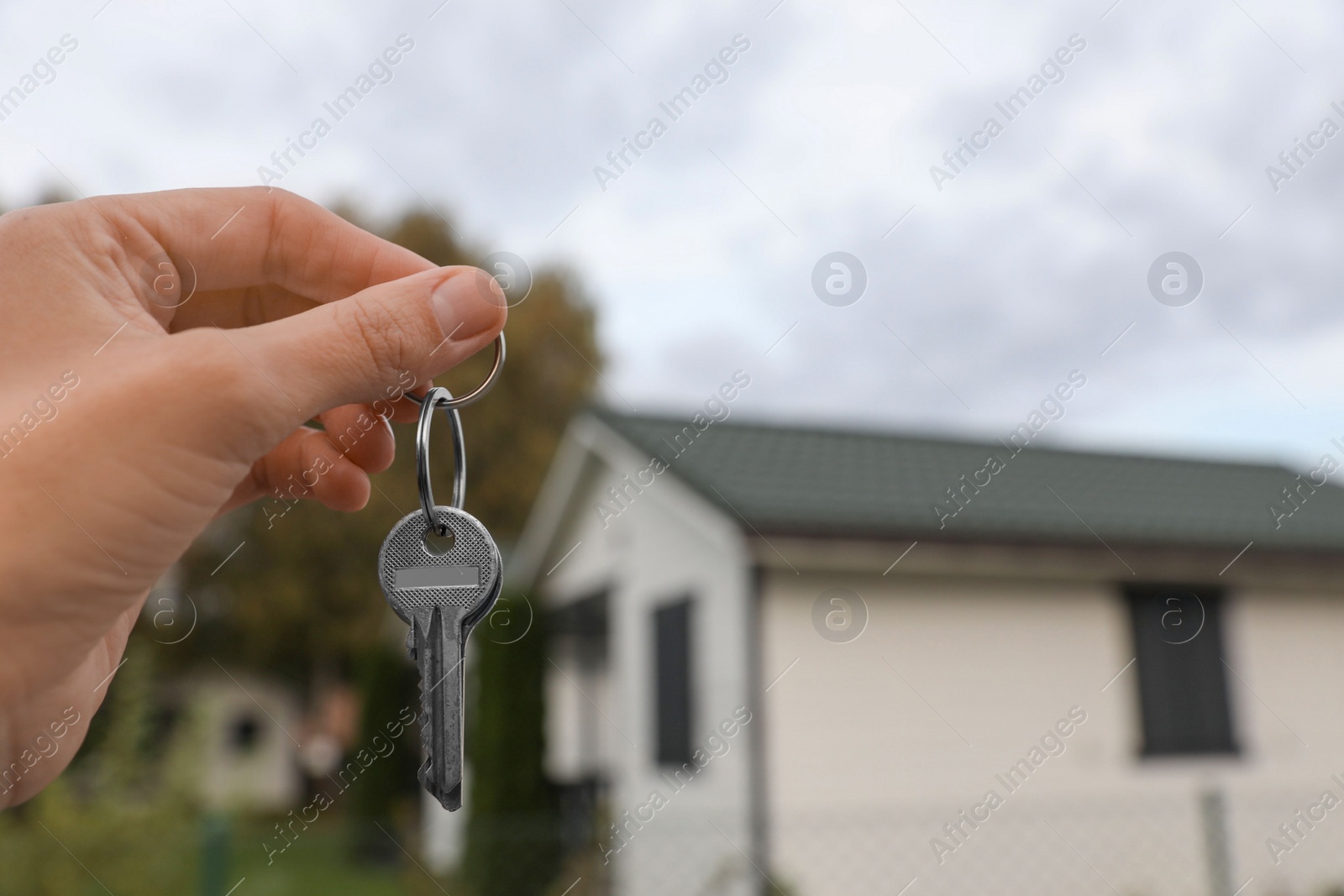 Photo of Real estate agent holding keys to new house outdoors, closeup. Space for text