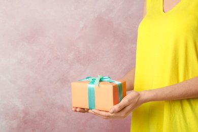 Woman holding beautifully wrapped gift box on color background