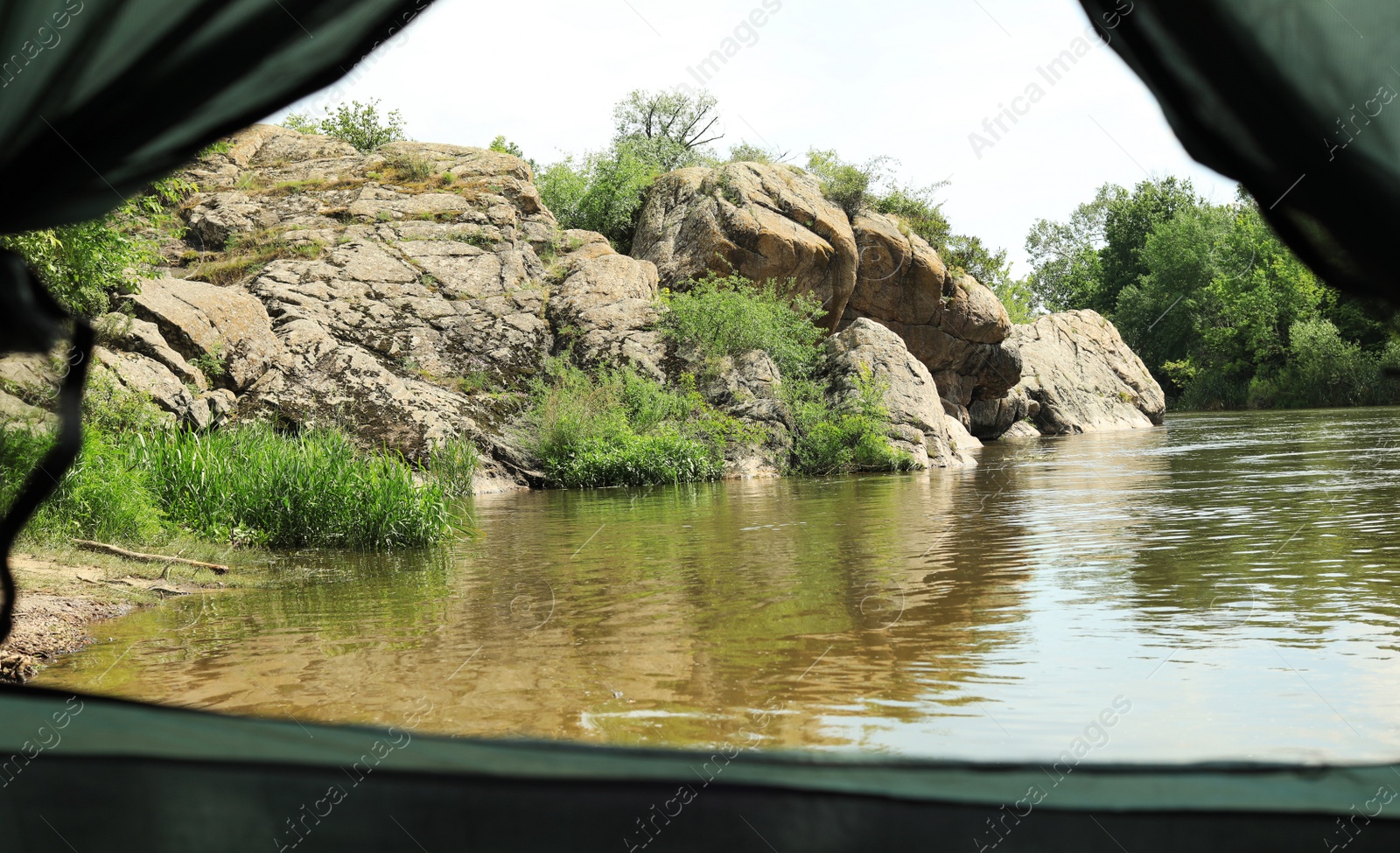 Photo of Calm river with rocky bank, view from camping tent