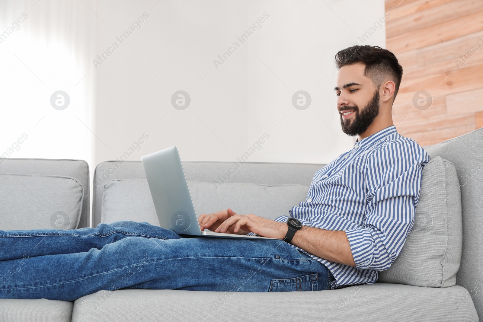 Photo of Handsome young man working with laptop on sofa at home