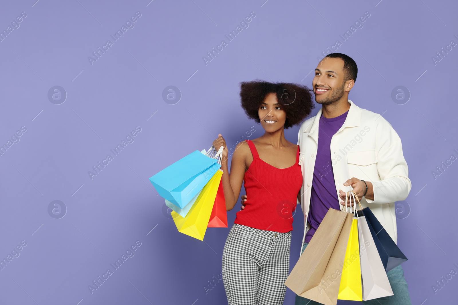 Photo of Happy African American couple with shopping bags on purple background. Space for text