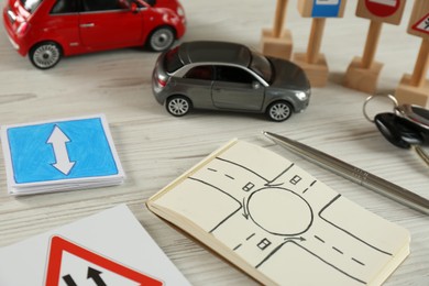 Photo of Composition with workbook for driving lessons and toy cars on white wooden background. Passing license exam