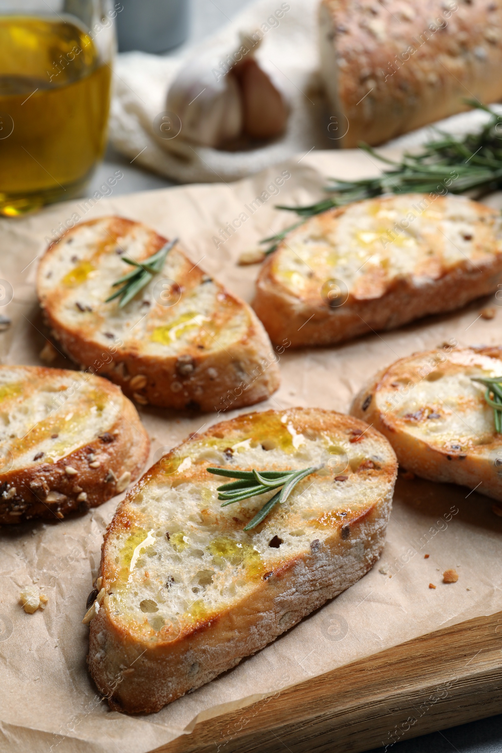 Photo of Tasty bruschettas with oil and rosemary on wooden board, closeup