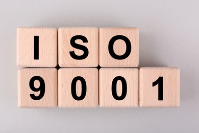 Photo of International Organization for Standardization. Wooden cubes with abbreviation ISO and number 9001 on light grey background, flat lay